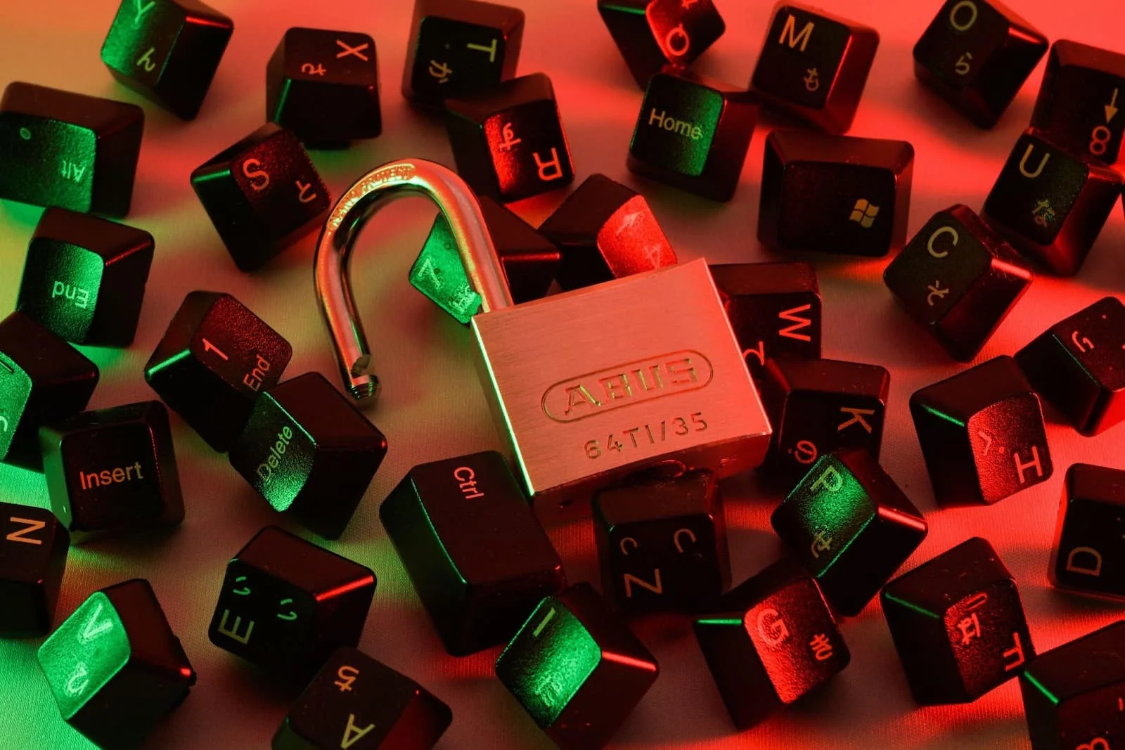 An open padlock lying among scattered keyboard keycaps, lit in red and green