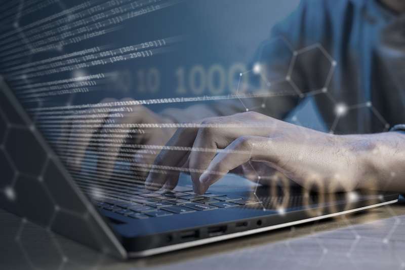 Hands typing on a laptop with lines of code, binary digits and a network lattice overlaid across the image