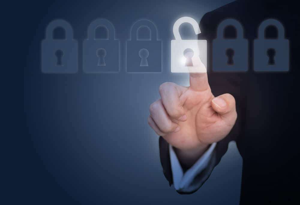 A hand reaching out to touch a glowing open padlock in a row of closed padlocks on a dark blue background