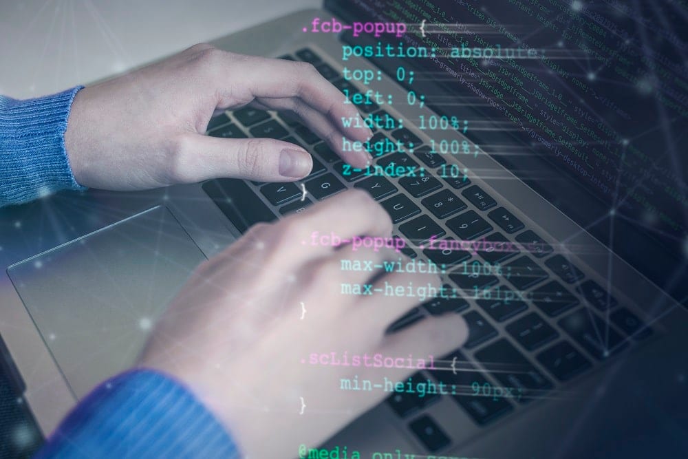 Unas manos teclean en un portátil con líneas de CSS superpuestas sobre la imagen