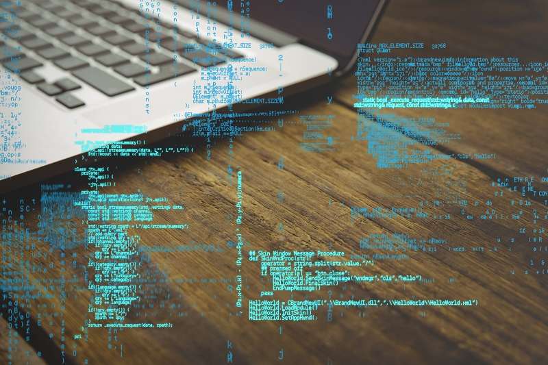 A laptop on a wooden desk with lines of code projected across the image in blue