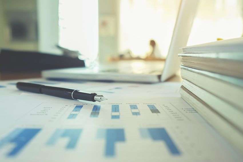 Una pluma estilográfica apoyada sobre un informe impreso con gráficos de barras, junto a una pila de documentos en un escritorio
